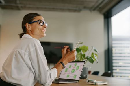 Mulher sorridente analisa gráficos em laptop, simbolizando planejamento estratégico para negócios lucrativos em 2025 no ambiente corporativo.