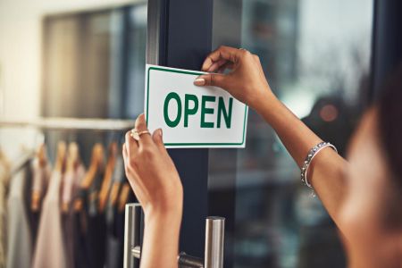mulher pendurando uma placa de "aberto" em sua loja no shopping após aprender como abrir uma loja de sucesso