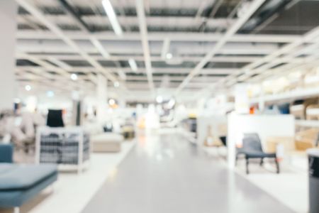 Vista interna desfocada de um amplo Showroom de móveis e decoração, apresentando iluminação clara e diversos produtos organizados em exposição.