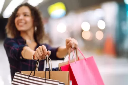 Mulher sorrindo segura sacolas de compras em corredor de shopping.