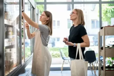 atendente de café mulher pegando item para a cliente em geladeira - tipos de clientes