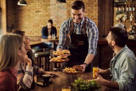 Garçom serve hambúrgueres e batatas fritas a clientes em uma das opções de franquias baratas de alimentação.